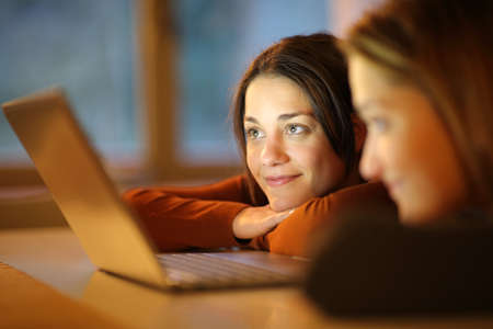 Two friends watching media content on laptop together in the night at homeの写真素材