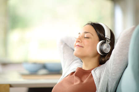 Carefree woman relaxing listening to music wearing headphones sitting on a sofa at homeの写真素材