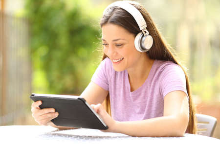 Happy woman with wireless headphones checking tablet content in a garden at homeの写真素材