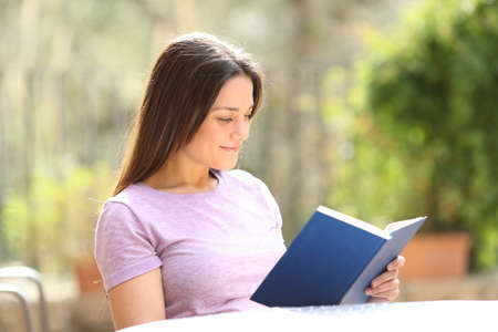 Satisfied woman reading a paper book sitting in a chair in a garden at homeの写真素材