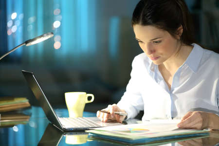 Businesswoman comparing inform on laptop working in the night at homeofficeの写真素材