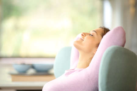 Side view of a satisfied tenant woman resting and relaxing on a couch at homeの写真素材