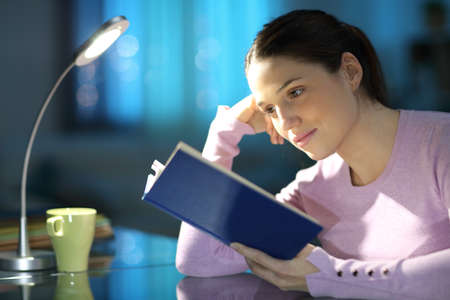 Concentrated woman reading a paper book at home in the nightの写真素材