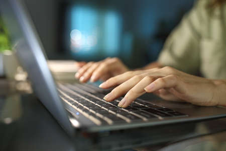 Close up of a woman hands typing on laptop keyboard in the night at homeの写真素材