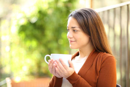 Satisfied woman drinking coffee looking away in a garden at homeの写真素材