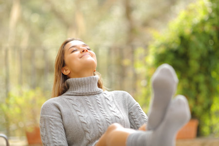 Happy woman resting seated in a chair breathing fresh air in a garden at home in winterの写真素材