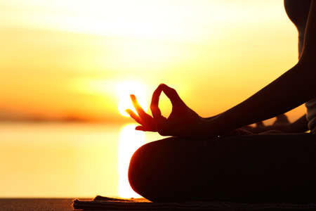 Backlight close up of woman silhouette doing yoga exercise at sunset on the beachの写真素材