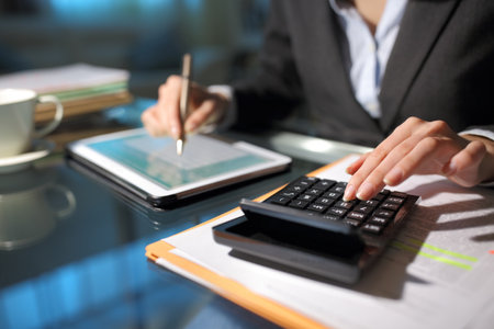 Close up of a businesswoman hands using tablet and calculator in the night at homeofficeの写真素材