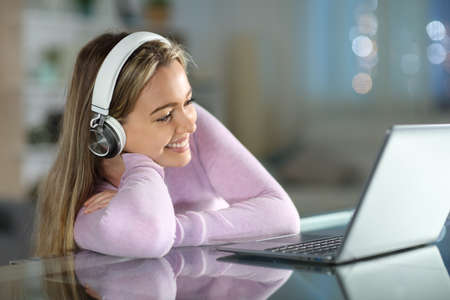 Happy teen watching videos on laptop in the night in the living room at homeの写真素材