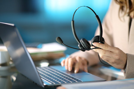 Close up of a tele marketer holding headset using laptop at homeofficeの写真素材