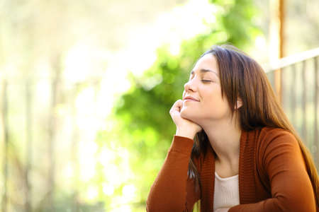 Satisfied woman relaxing with closed eyes breathing fresh air in a garden at homeの写真素材