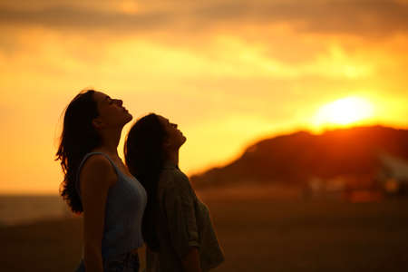 Profile of two women silhouette breathing fresh air at sunset on the beachの写真素材