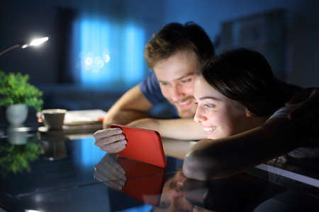 Happy couple watching media together on smart phone in the night at homeの写真素材