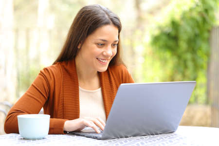 Happy woman browsing laptop content outdoors in a house terraceの写真素材