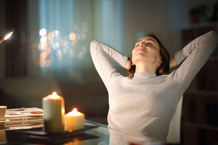 Relaxed woman resting sitting on a chair in the night with candles at homeの写真素材