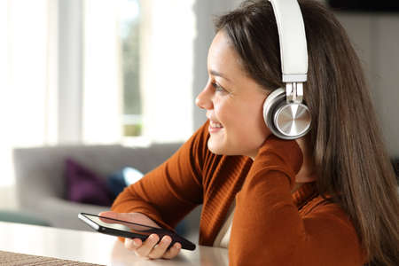 Happy lady with wireless headphones listening to music with smart phone at homeの写真素材