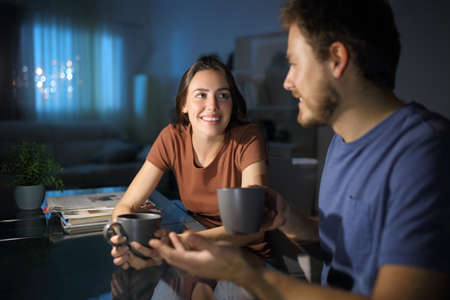 Happy couple talking in the night in the living room at homeの写真素材