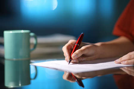 Close up of a woman hand filling out paper form in the night at homeの写真素材