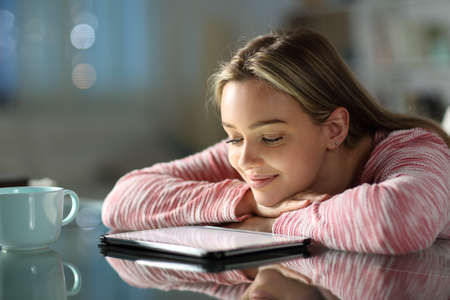 Happy teen watching online videos on tablet on a table in the night at homeの写真素材