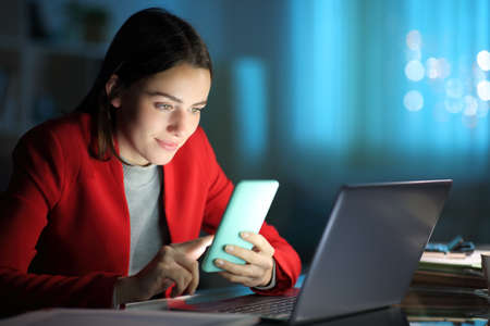 Concentrated entrepreneur using mobile phone and laptop in the night at homeの写真素材
