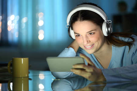 Happy woman watching online videos on smartphone in the night at homeの写真素材