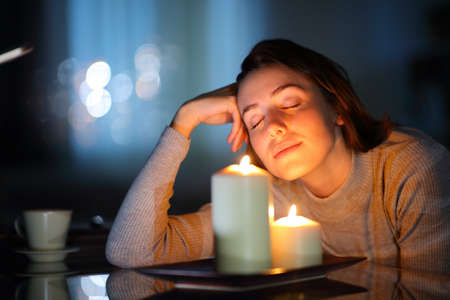 Relaxed woman smelling aromatic candles in the night in the living room at home