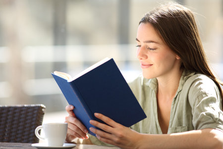 Satisfied woman reading a paper book sitting in a coffee shopの写真素材