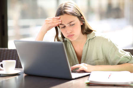 Overwhelmed student e-learning complaining looking at notes in a coffee shopの写真素材