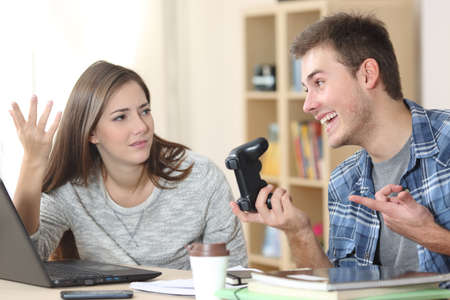 Angry student girl complaining to lazy classmate waiting to do homework at homeの写真素材
