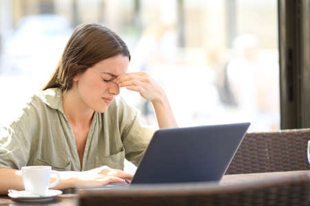 Fatigued woman suffering eyestrain working with a laprop sitting in a coffee shopの写真素材