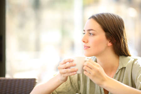 Relaxed woman drinking coffee from mug looking at side in a barの写真素材