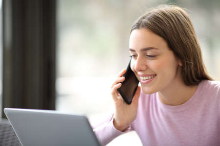 Happy woman with laptop talking on mobile phone in a coffee shop or apartmentの写真素材