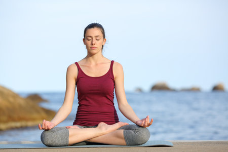Front view portrait of a concentrated woman doing yoga exercise on the beachの写真素材