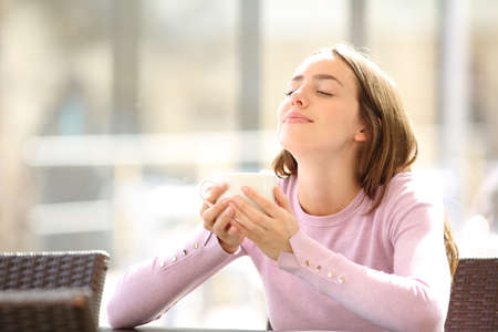 Relaxed woman holding coffee cup breathing fresh air in a bar terraceの写真素材