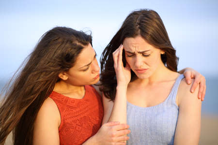 Sad woman complaining being comforted by her friend on the beachの写真素材