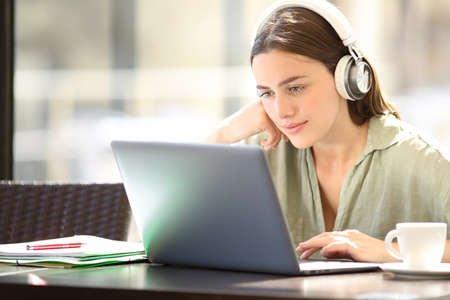 Satisfied woman e-learning with laptop and headphones sitting in a barの写真素材