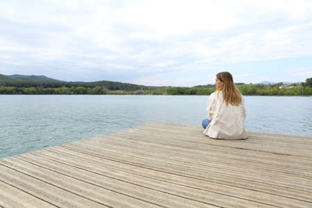 Woman resting contemplating views sitting in a pier in a lakeの写真素材