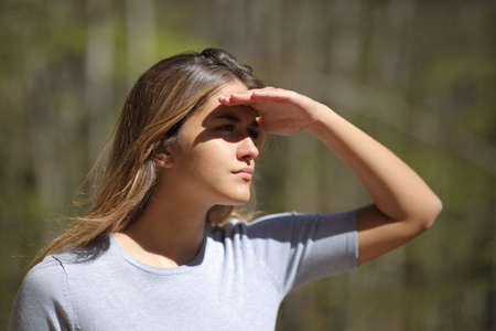 Woman protecting from sun with her hand looking away in a forestの写真素材