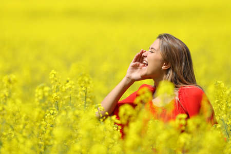 Happy woman shouting with hand on mouth in a yellow field in spring seasonの写真素材