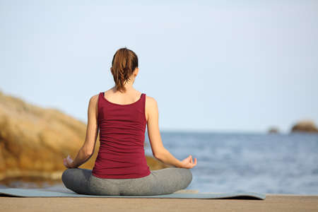 Back view full body portrait of a woman doing yoga exercise on the beachの写真素材