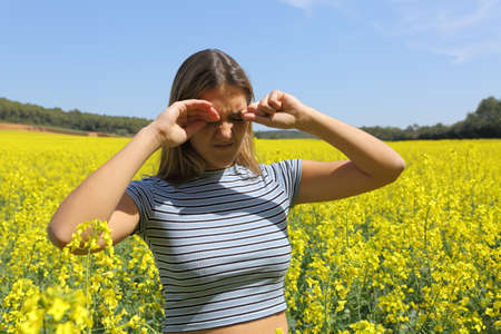 Stressed woman scratching itchy eyes in a crop field in spring seasonの写真素材