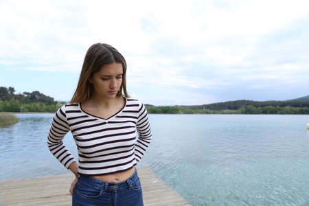 Sad woman walking alone towards camera in a pier of a lakeの写真素材