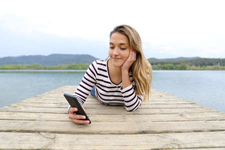 Front view portrait of a relaxed woman checking smart phone in a lake pierの写真素材