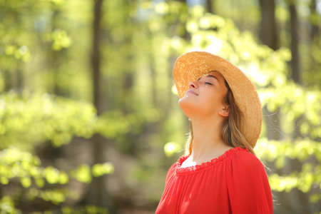 Happy woman in red wearing pamela breathing fresh air in a green forestの写真素材