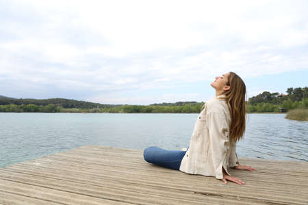 Relaxed woman sitting in a pier breathing fresh air in a lakeの写真素材