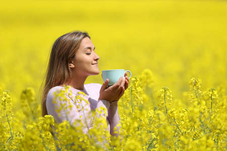 Side view portrait of a woman drinking coffee in the middle of a yellow field in spring seasonの写真素材