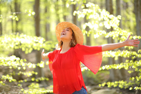 Excited woman spreading happiness outstretching arms in a green forest a sunny dayの写真素材