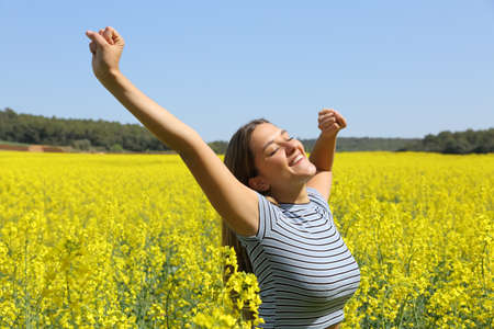 Happy woman stretching arms in a yellow flowered field in spring seasonの写真素材