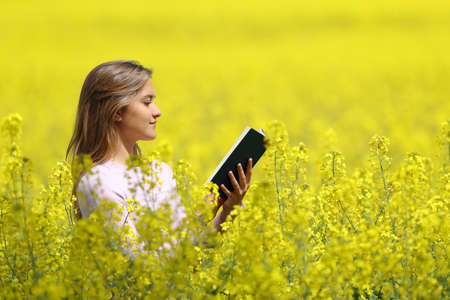 Side view portrait of a woman reading a paper book in a yellow field in springの写真素材