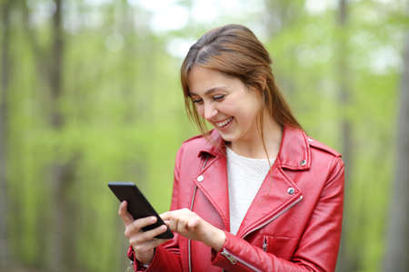 Happy woman in red using mobile phone standing in a green forestの写真素材